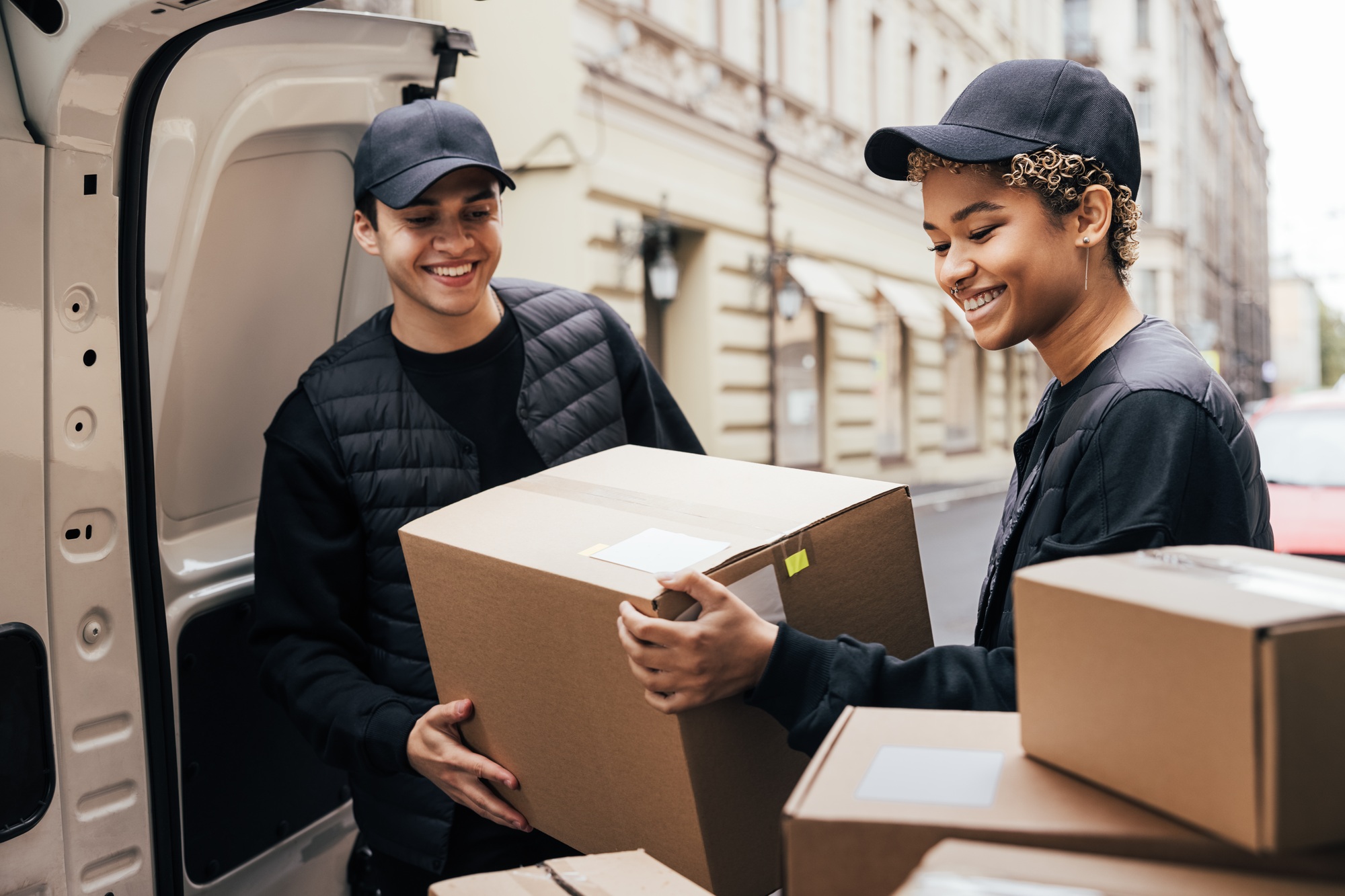 two-smiling-couriers-unloading-cardboard-boxes-from-van-in-the-city.jpg